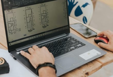 An architect working on building designs using a laptop outdoors, highlighting modern architecture.